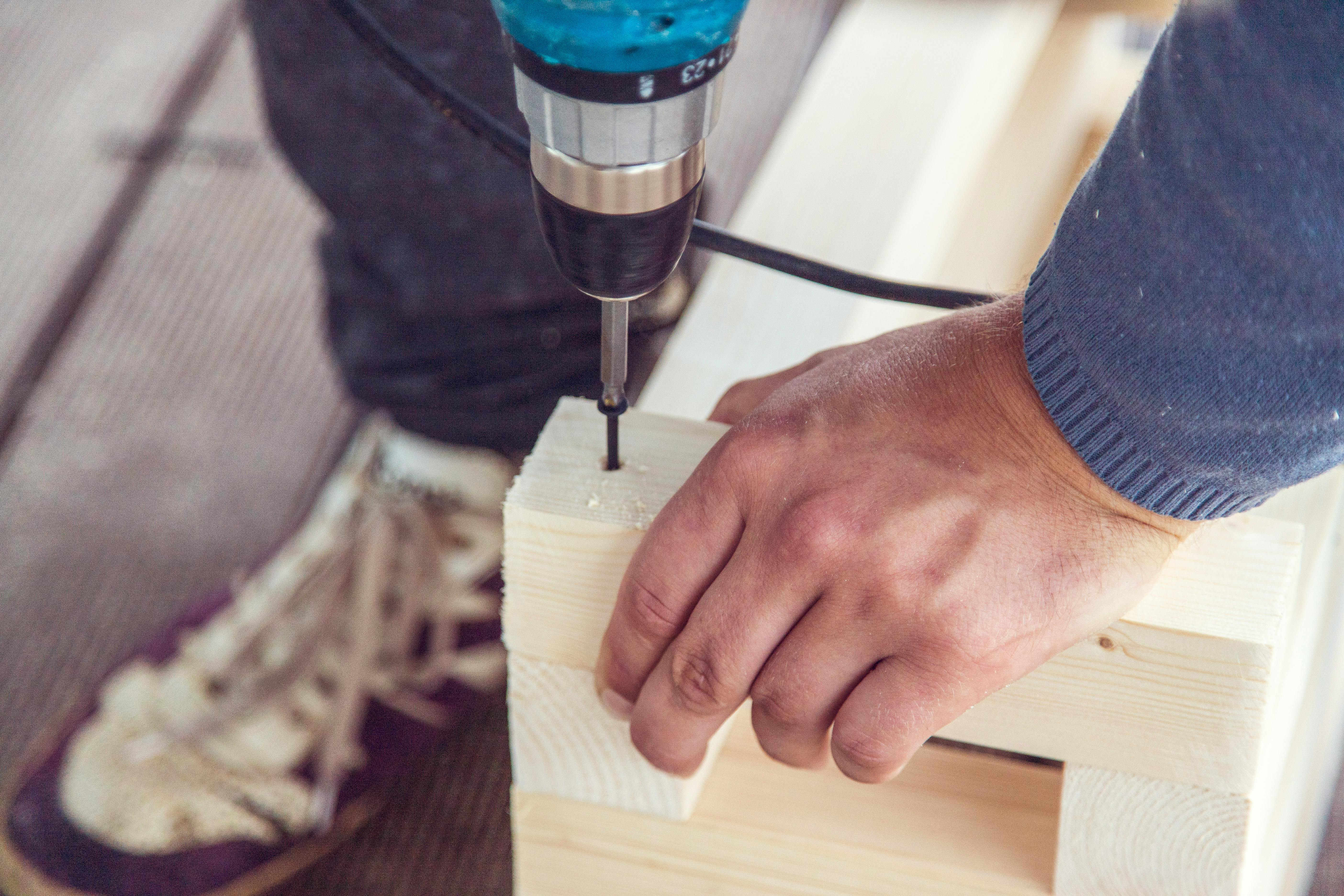 From above crop anonymous woodworker drilling hole with nail in wooden detail in workshop